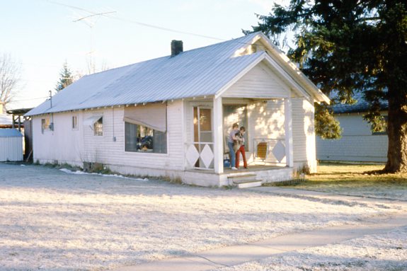 The parsonage (house owned by Church) is a white house with blue roof. It has a front porch. Tom and Bill are on the front porch with our dog, Cookie.