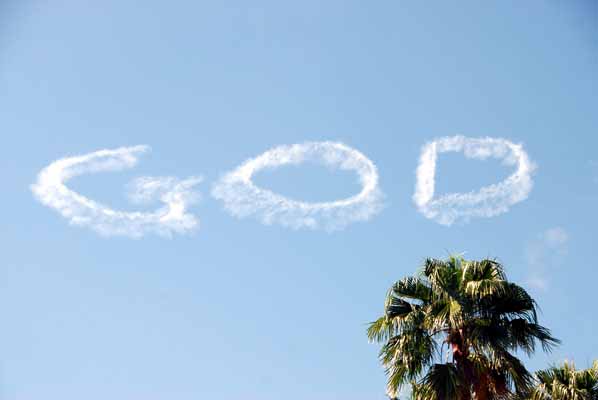 The word, God, written in white sky-writing, in blue sky with palm tree in bottom of picture.