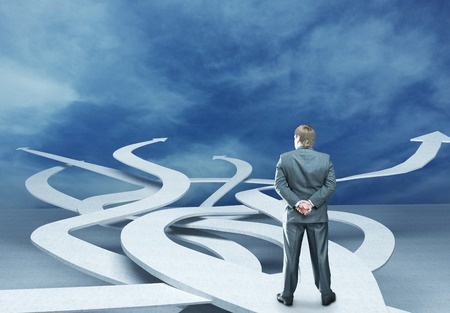 Man in suit standing on a road that separates into many directions. He needs to make a decision.