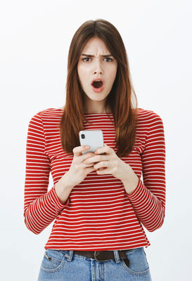 A young woman looks whiny. She has a phone in her hands. She has long brown hair and is wearing a red striped shirt and blue jeans.
